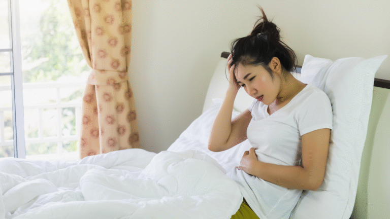 Woman holding her stomach and looking uncomfortable in bed, showing signs of poor gut health.