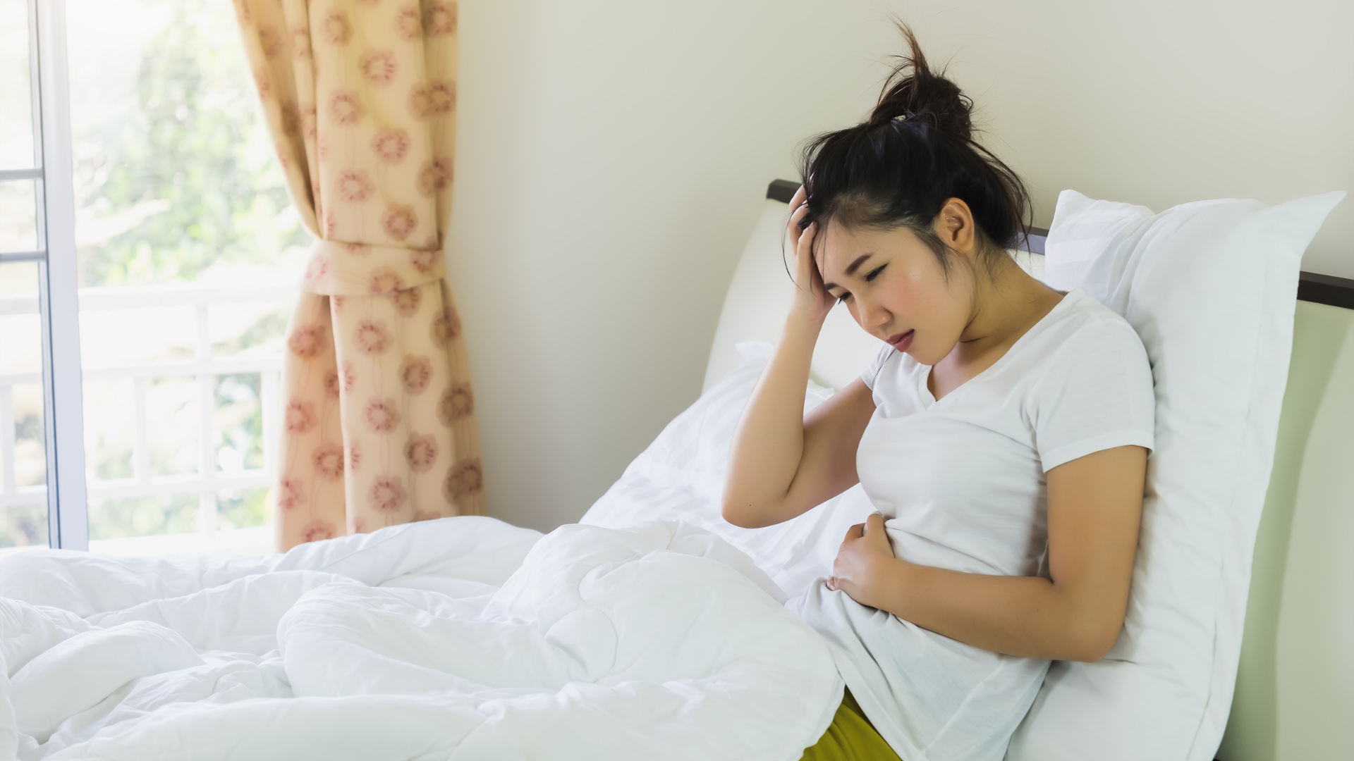 Woman holding her stomach and looking uncomfortable in bed, showing signs of poor gut health.