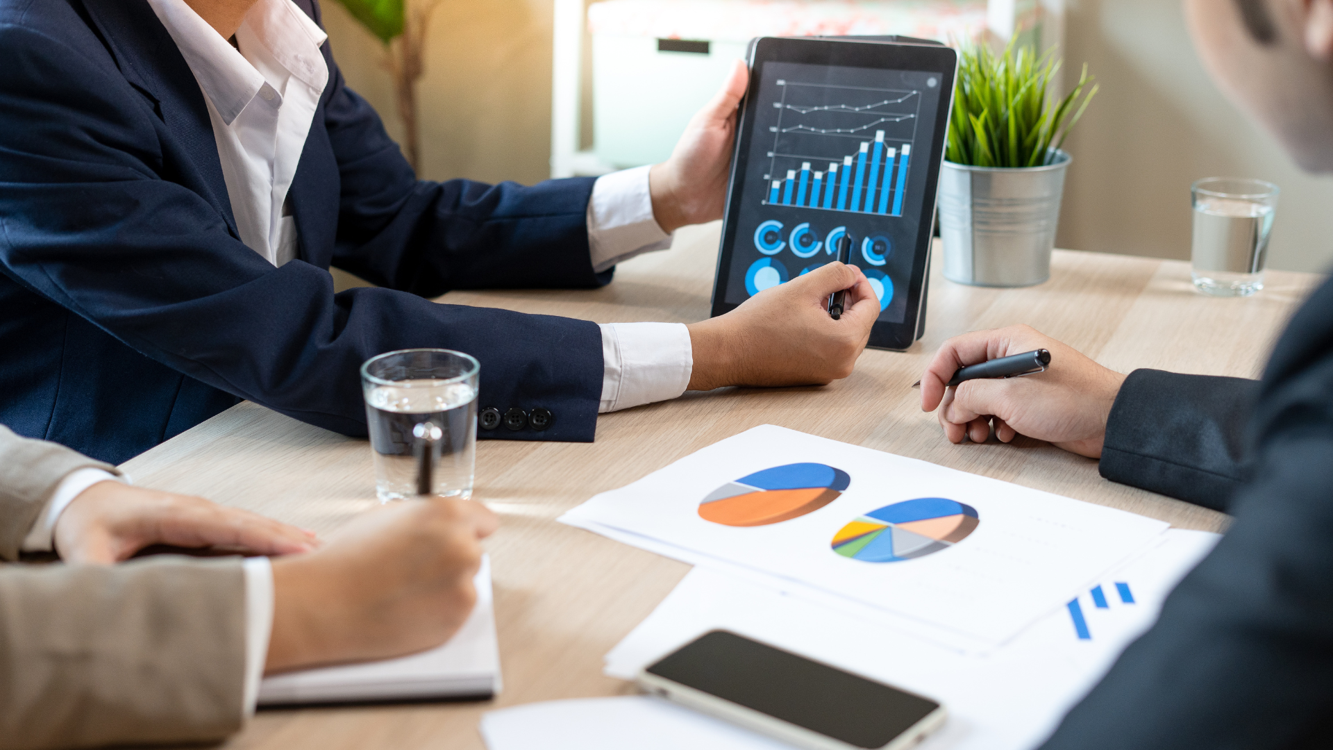 Financial advisor presenting business growth charts on a tablet during a meeting with clients.