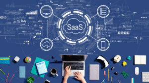 Top view of a workspace with a person typing on a laptop, surrounded by office supplies and tech gadgets, with digital graphics representing SaaS (Software as a Service) business technology, including cloud storage, data analysis, and device connectivity icons.