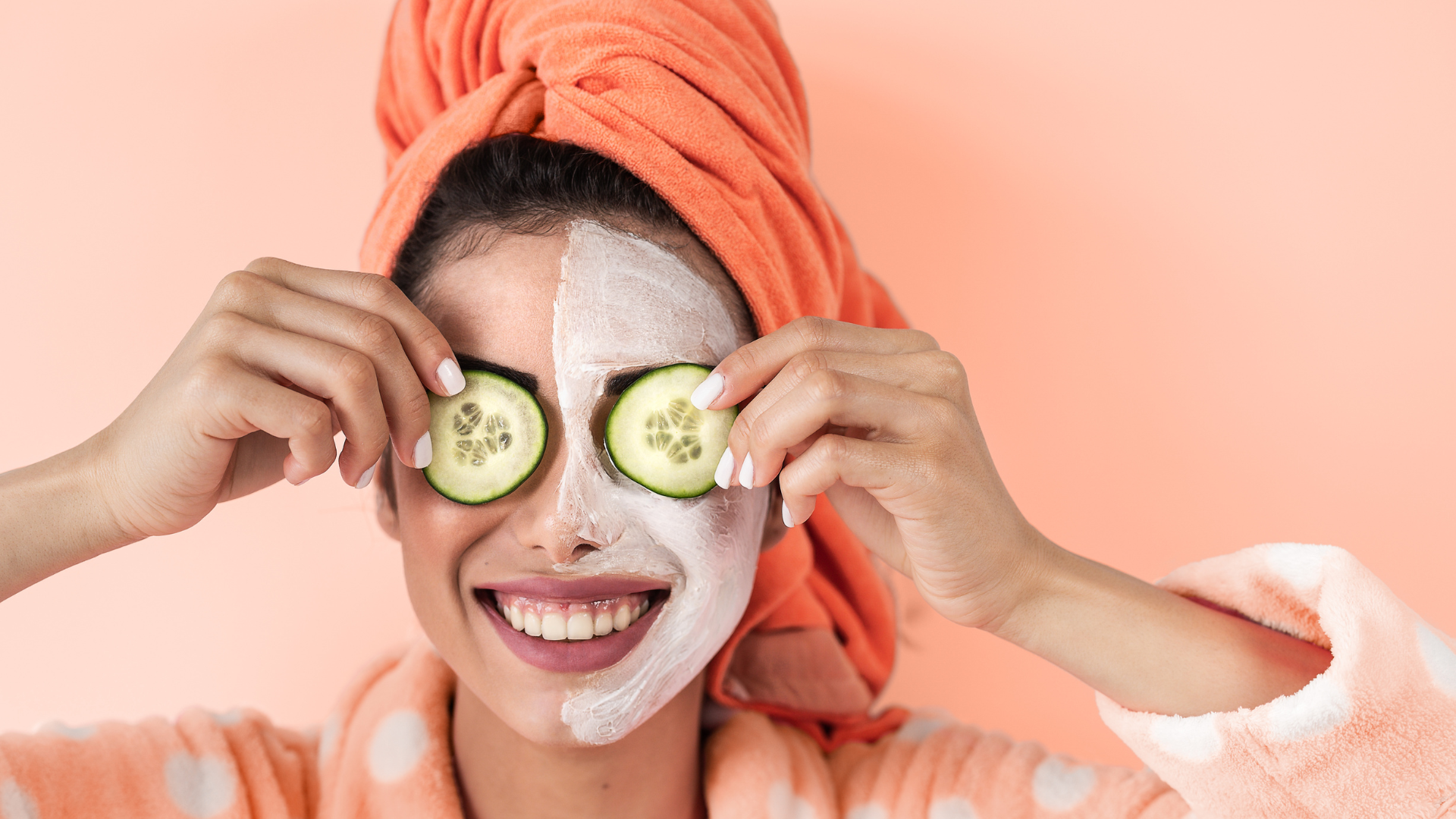A smiling woman in a bathrobe with a facial mask, holding cucumber slices over her eyes — representing skincare trends in 2025.