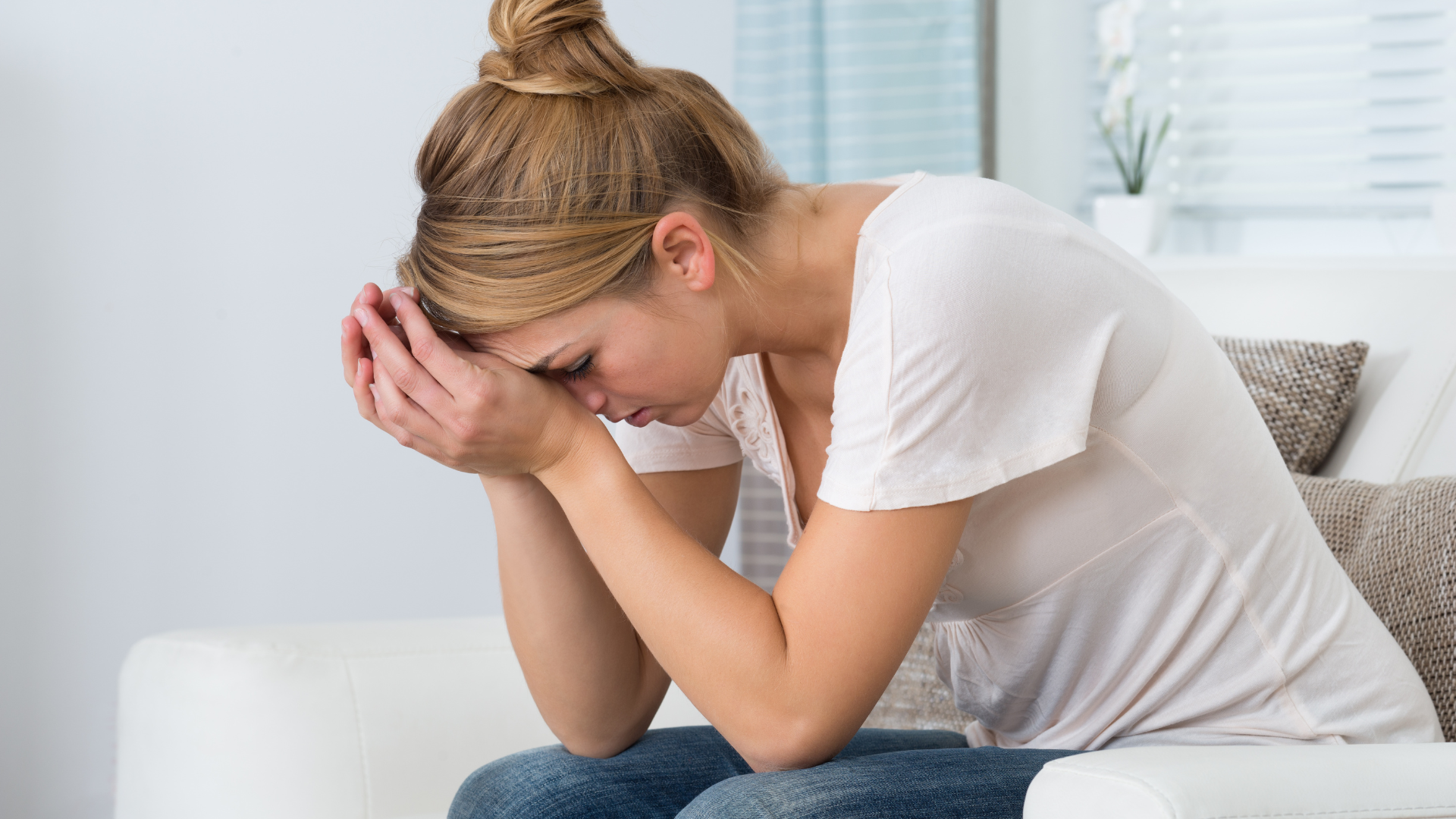 Stressed woman sitting on a couch with her head in hands, showing signs of stress and anxiety