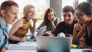 College students collaborating with laptops and books, engaging in microlearning activities through group study and digital tools.