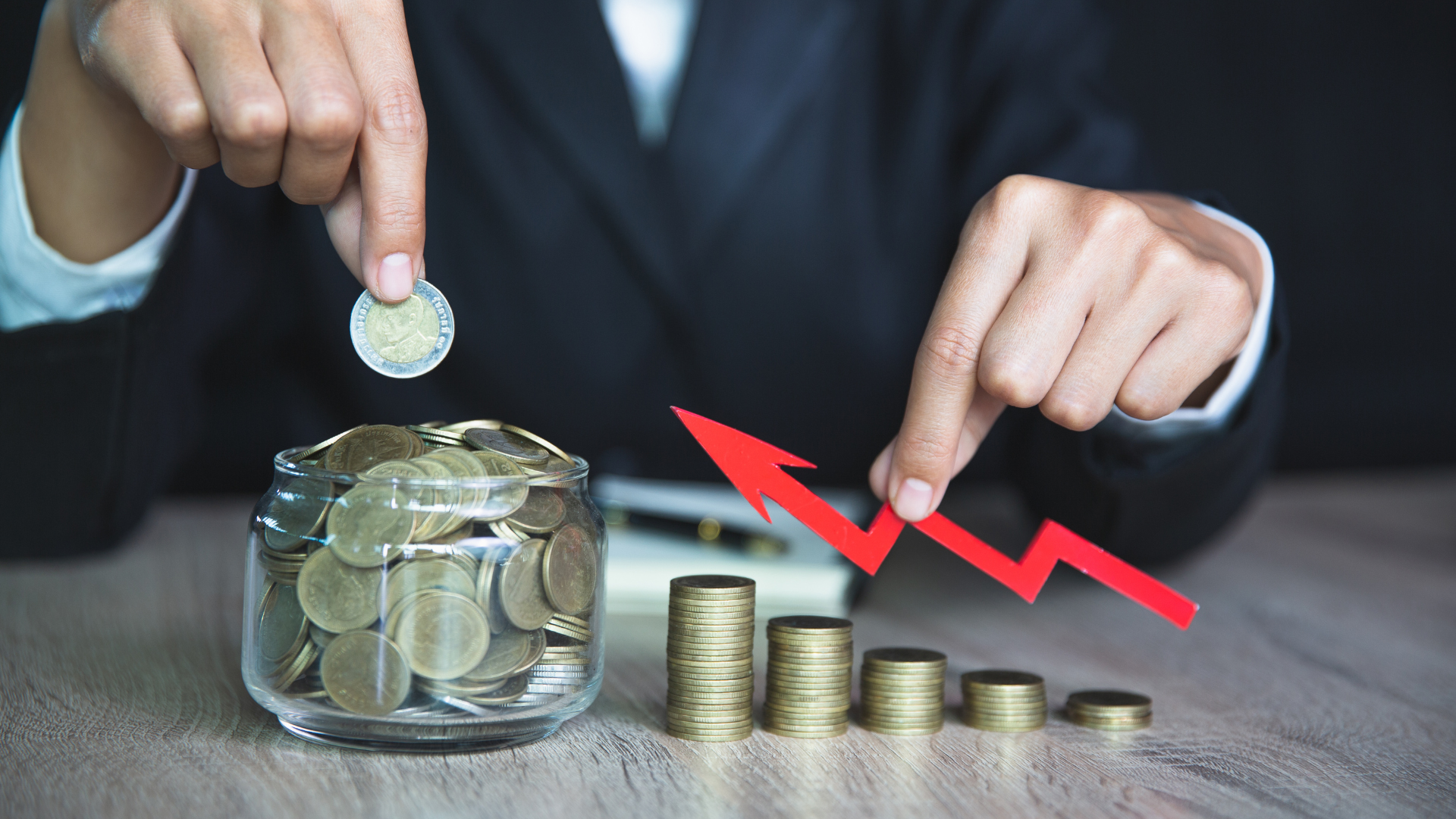 Business person stacking coins and pointing at growth arrow to symbolize how to build wealth through saving and investment.