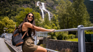Smiling solo traveler with a backpack enjoying scenic travel destinations near a waterfall and mountains.