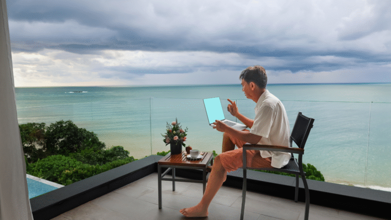 Digital nomad working remotely on a laptop with ocean view balcony, blending work and travel lifestyle.