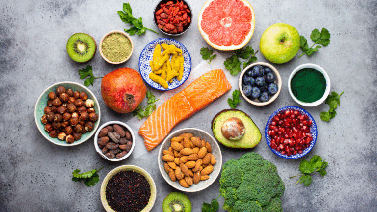 Assorted superfoods including salmon, avocado, nuts, berries, pomegranate, broccoli, and seeds arranged on a table for a healthy diet.