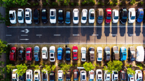Aerial view of a parking lot filled with modern fuel-efficient cars parked in rows surrounded by greenery.