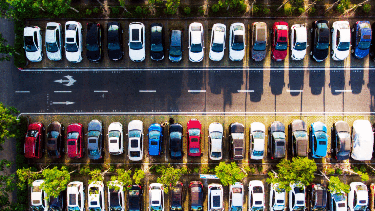 Aerial view of a parking lot filled with modern fuel-efficient cars parked in rows surrounded by greenery.