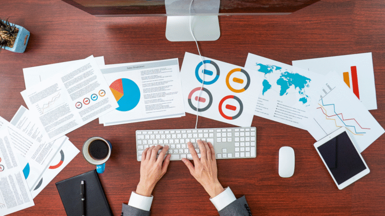 Business professional analyzing data analytics reports on a desktop with charts, graphs, and global metrics on the desk.