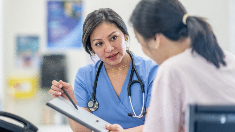A female healthcare professional in blue scrubs with a stethoscope around her neck explains information on a clipboard to a patient, illustrating the importance of addressing common health myths through accurate medical advice