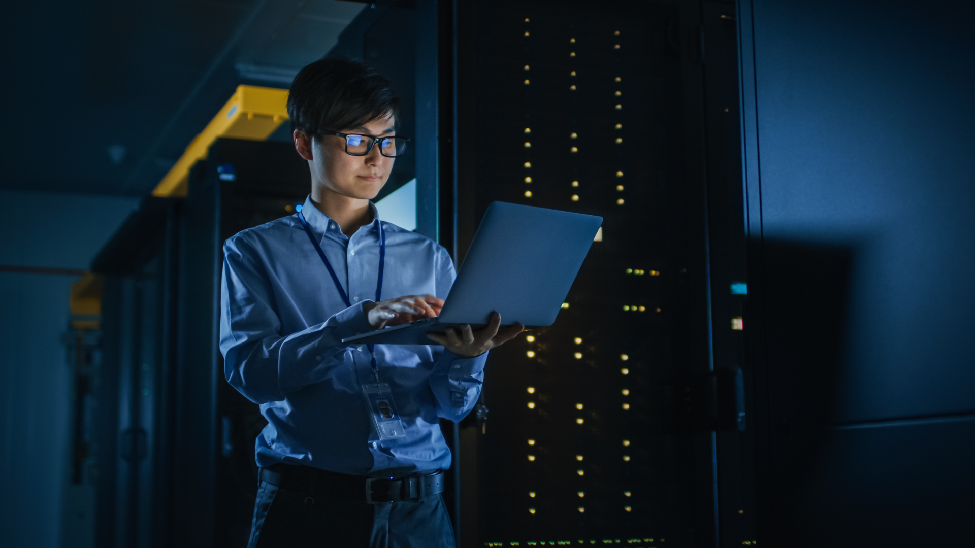 IT professional checking cybersecurity measures on a laptop in a server room with active data servers in the background