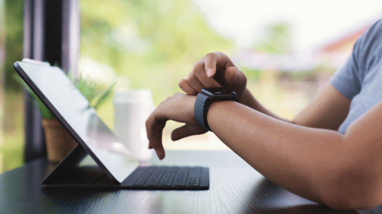 Person using wearable tech smartwatch while working on a tablet at a desk.