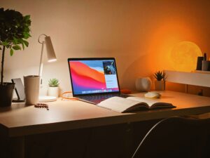 A MacBook Air on a desk with a glowing moon lamp and an open book, creating a cozy and productive workspace.