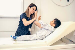 A cheerful pediatrician high-fives a young boy with a leg brace on an examination table, both smiling.