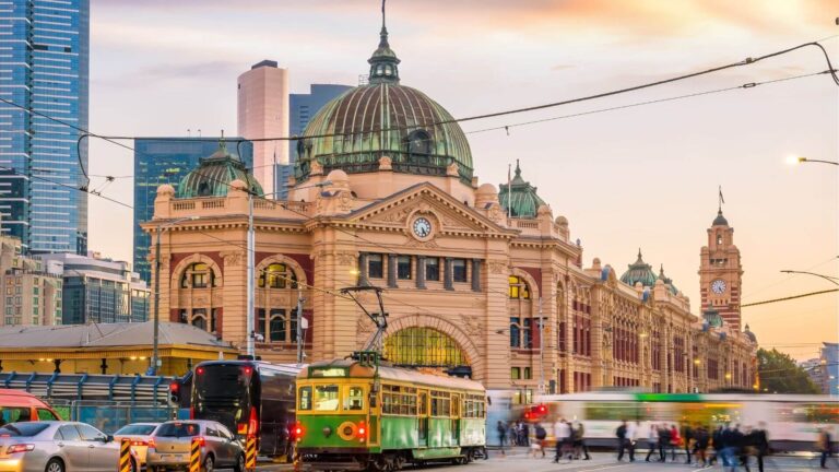 Flinders Street Station, a historic landmark in Melbourne, with trams and buses indicating options for sustainable travel and public transit.