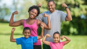 A happy family flexing their arms outdoors, showing how people can stay fit through simple, active lifestyle habits without needing a gym.