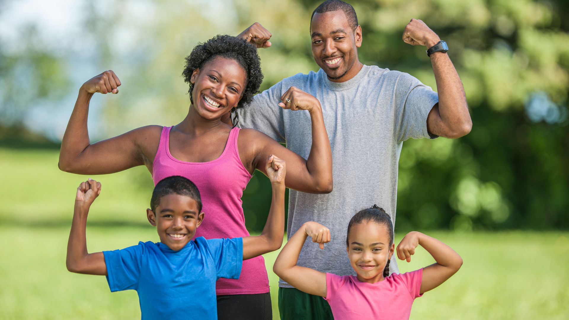 A happy family flexing their arms outdoors, showing how people can stay fit through simple, active lifestyle habits without needing a gym.