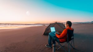 A remote worker using a laptop on a beach beside a tent during sunset, representing the freedom and lifestyle associated with top digital nomad cities around the world.