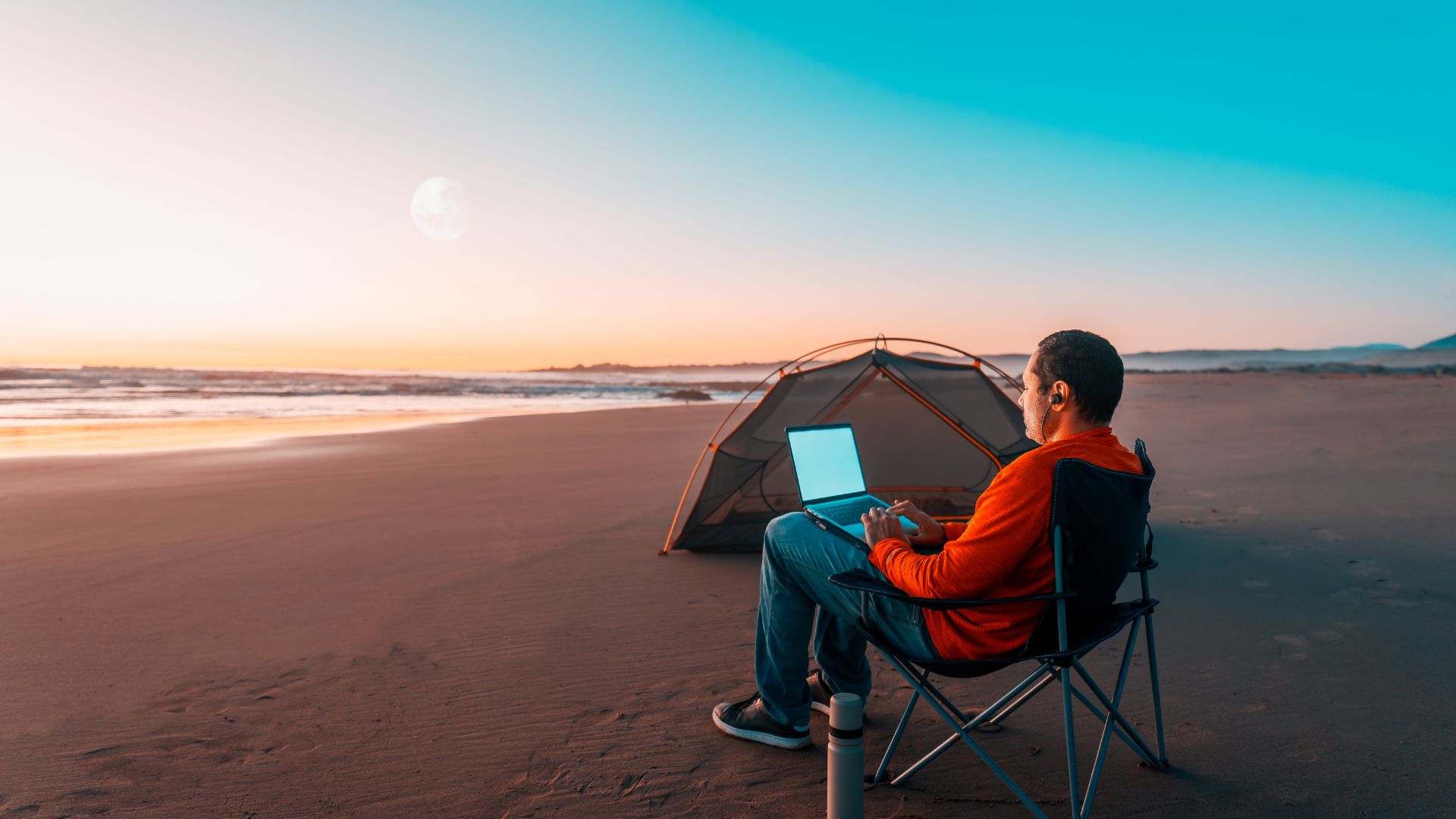 A remote worker using a laptop on a beach beside a tent during sunset, representing the freedom and lifestyle associated with top digital nomad cities around the world.