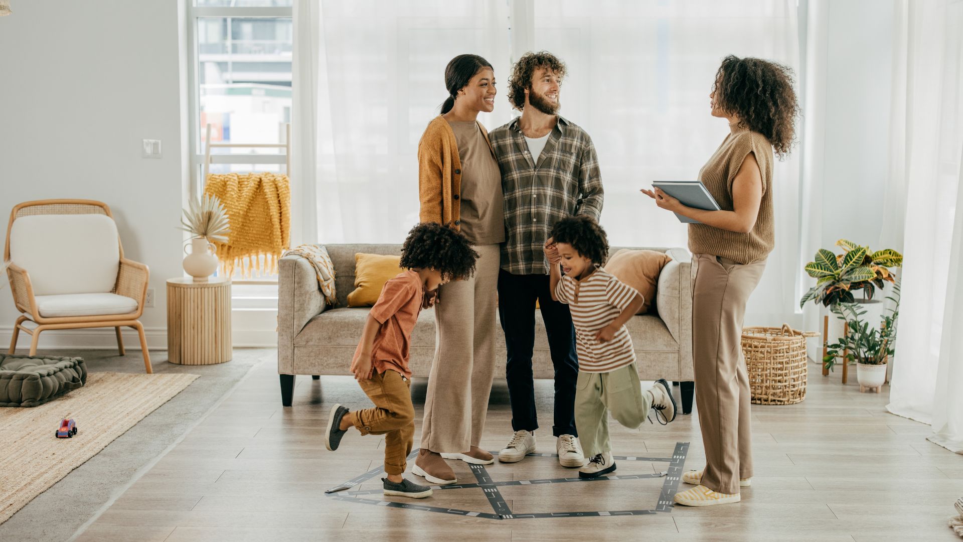 A family touring a bright living room with a real estate agent, illustrating the Renting vs Buying decision process as they explore potential homes.