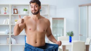 A man showing significant weight loss by wearing oversized jeans, symbolizing modern Weight Loss Trends and the impact of effective fitness and diet strategies.