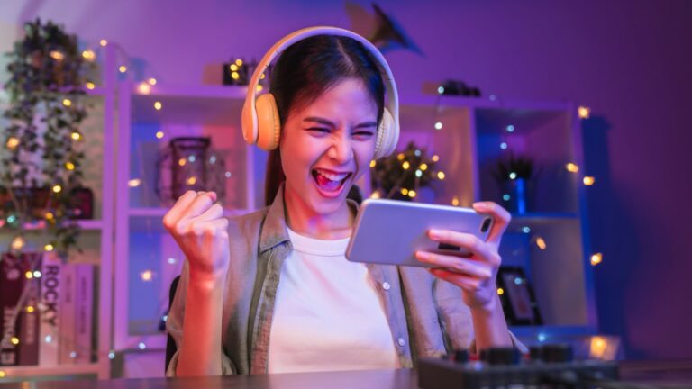 A woman celebrating while playing mobile games on her phone, enjoying an immersive gaming experience with headphones on.