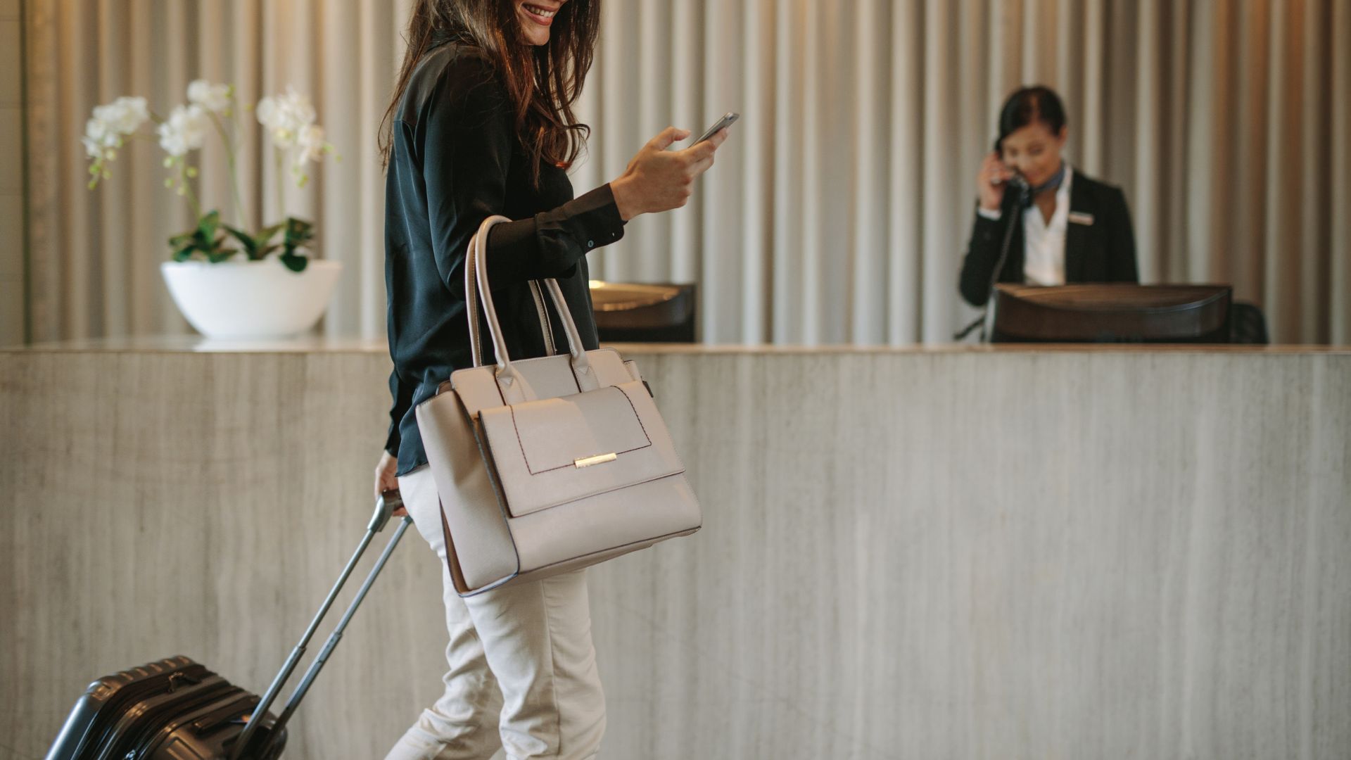 A solo woman traveler checking her phone at a hotel reception, representing the use of travel apps for solo women.