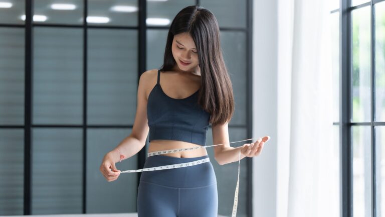 A woman measuring her waist, representing how to lose weight without gym through simple home routines.