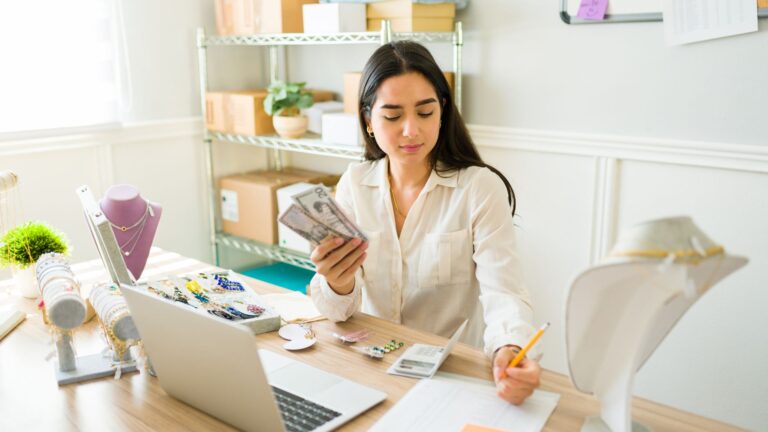 A woman counting cash at her desk while running an online business, representing ways to make money online.