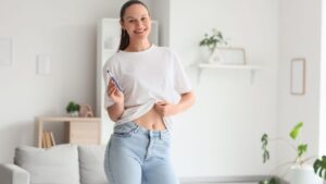 A woman smiling while using an injection pen at home, symbolizing balanced hormone health and self-care for overall wellness.