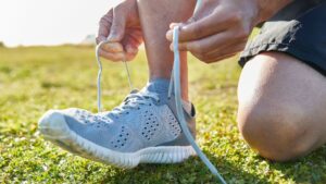 Person tying the laces of their running shoes outdoors on a grassy field, preparing for a run.
