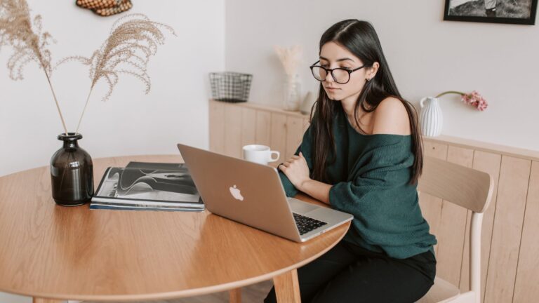 Young woman working on a laptop at home, researching freelancing opportunities online.
