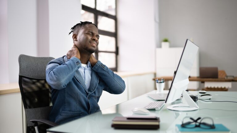 Why Sitting All Day Causes Neck and Back Pain (And How to Fix It) – office worker holding neck due to prolonged desk work