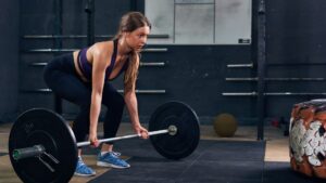Beginner woman learning how to start gym training while performing a deadlift with proper form in a fitness center.
