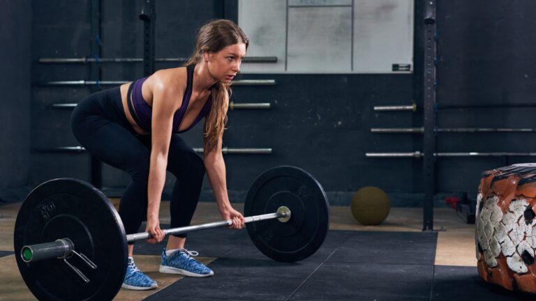 Beginner woman learning how to start gym training while performing a deadlift with proper form in a fitness center.