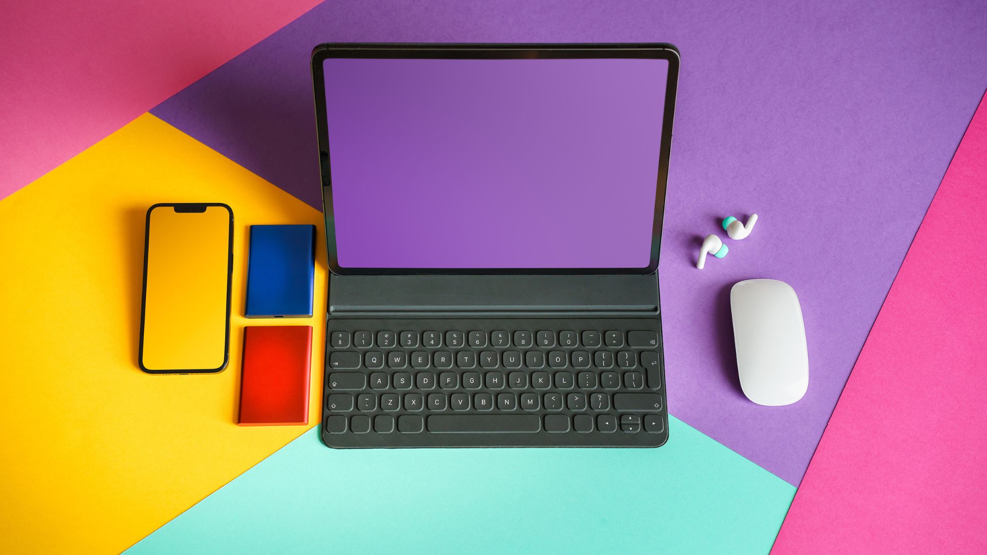 Flat lay of modern tech gadgets including a tablet with keyboard, smartphone, storage drives and accessories representing the best laptops and devices for 2026.