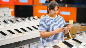 Woman checking smartphones in an electronics store while researching if buying a refurbished phone is worth it in 2026