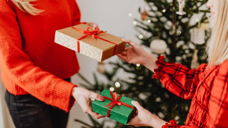 Two people exchanging Christmas gifts in front of a decorated Christmas tree