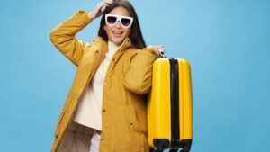 Woman posing with a yellow suitcase while exploring whether travel packages are worth it or a waste of money in 2026