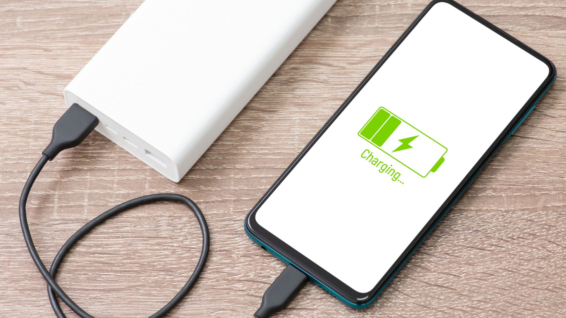 Smartphone charging from a power bank on a wooden table.