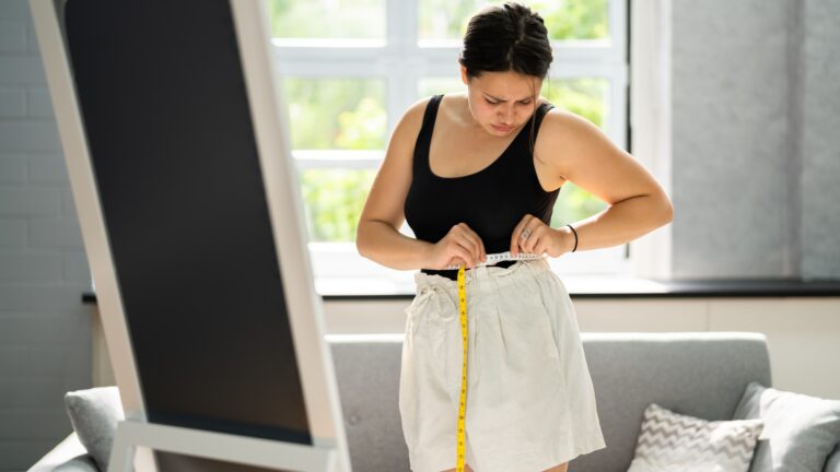 Woman measuring waist with tape at home, illustrating fat loss vs weight loss and body composition changes