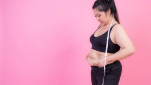 Woman measuring belly fat with a tape measure, showing abdominal fat concerns during a weight loss journey.