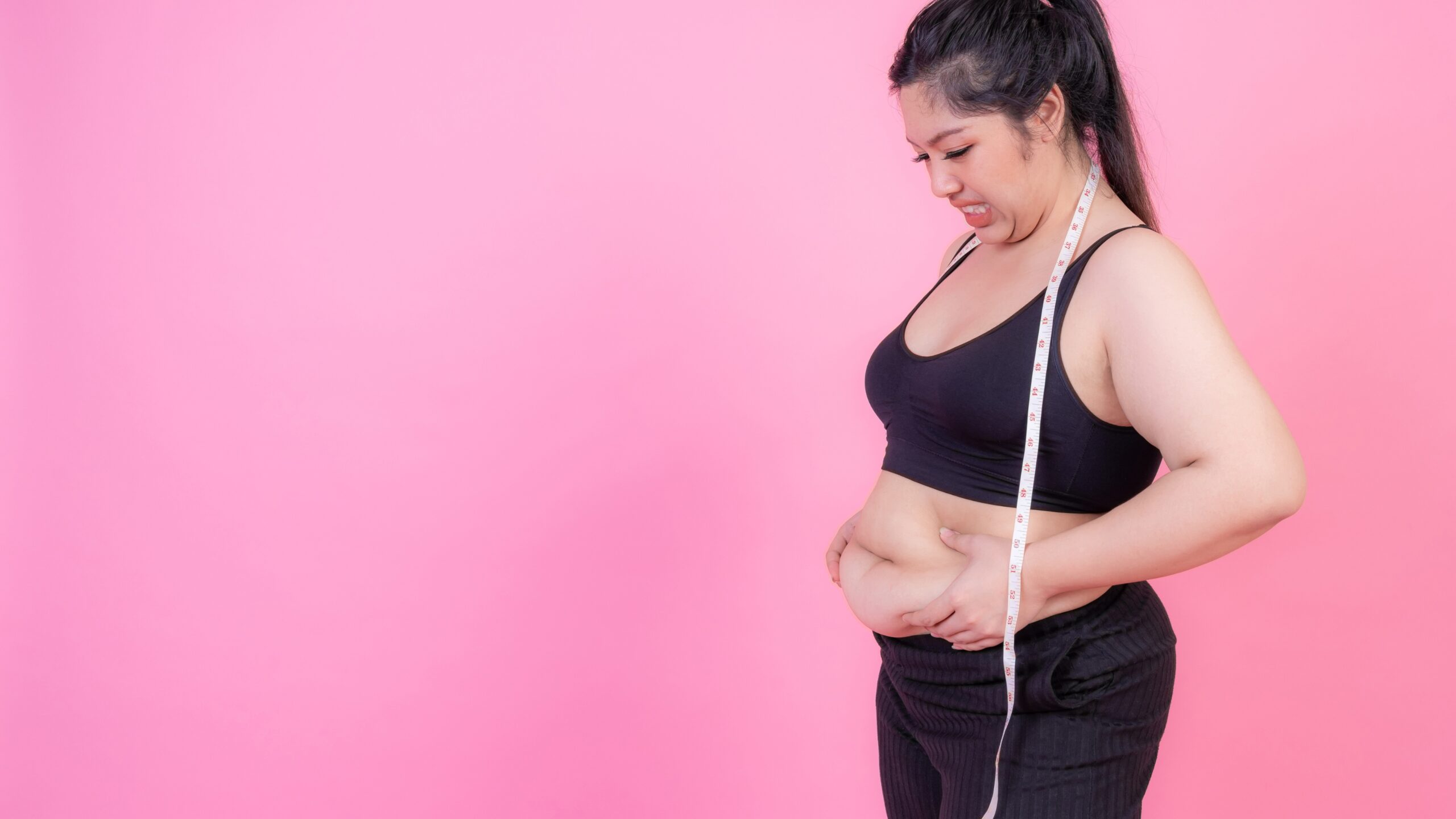 Woman measuring belly fat with a tape measure, showing abdominal fat concerns during a weight loss journey.