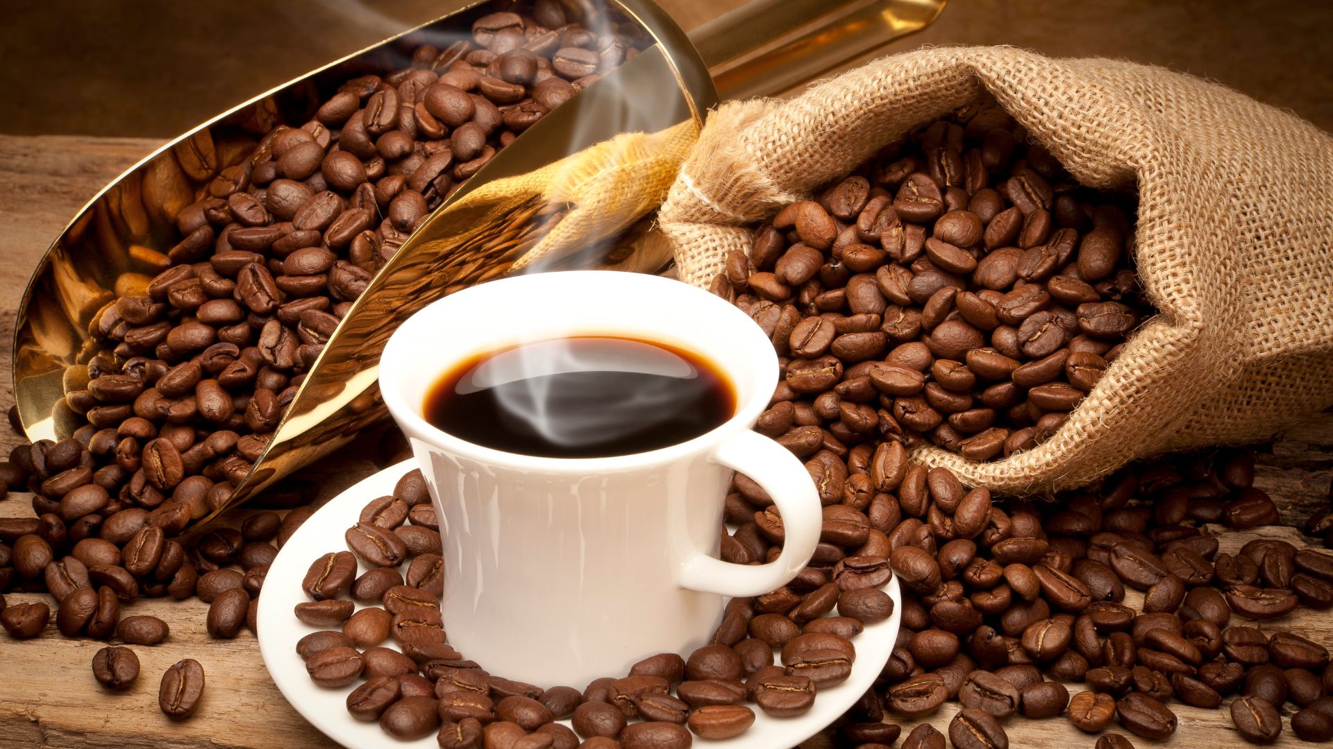 A steaming cup of black coffee surrounded by roasted coffee beans, illustrating discussions about whether drinking coffee at night affects sleep.