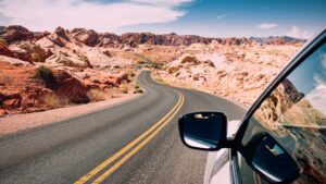 Road trips through a scenic desert landscape, view from inside a car driving along a winding highway surrounded by rocky canyons and open skies, capturing the freedom of long-distance travel.