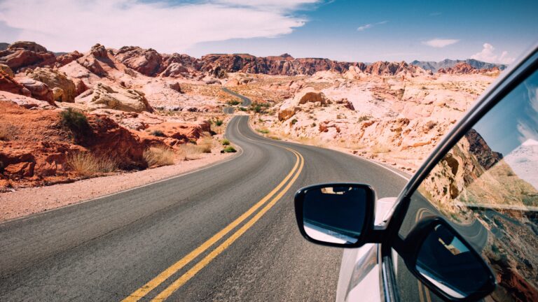 Road trips through a scenic desert landscape, view from inside a car driving along a winding highway surrounded by rocky canyons and open skies, capturing the freedom of long-distance travel.