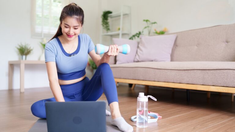 Woman following budget-friendly home workout plans using a laptop and dumbbells in her living room