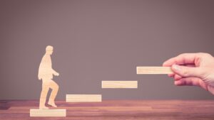 Wooden figure stepping up blocks, symbolizing career switch guides: from office job to creative fields