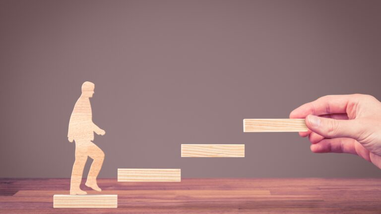 Wooden figure stepping up blocks, symbolizing career switch guides: from office job to creative fields